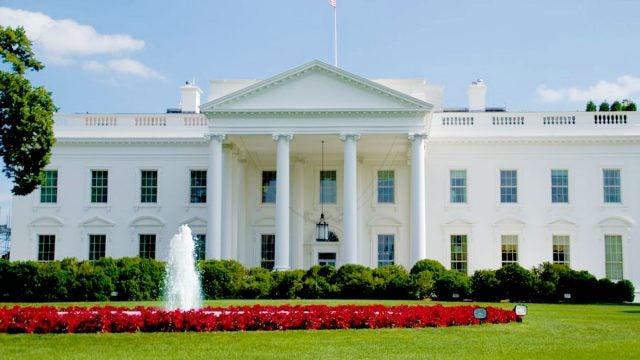 The White House stands with a ring of red flowers surrounding a fountain in front.