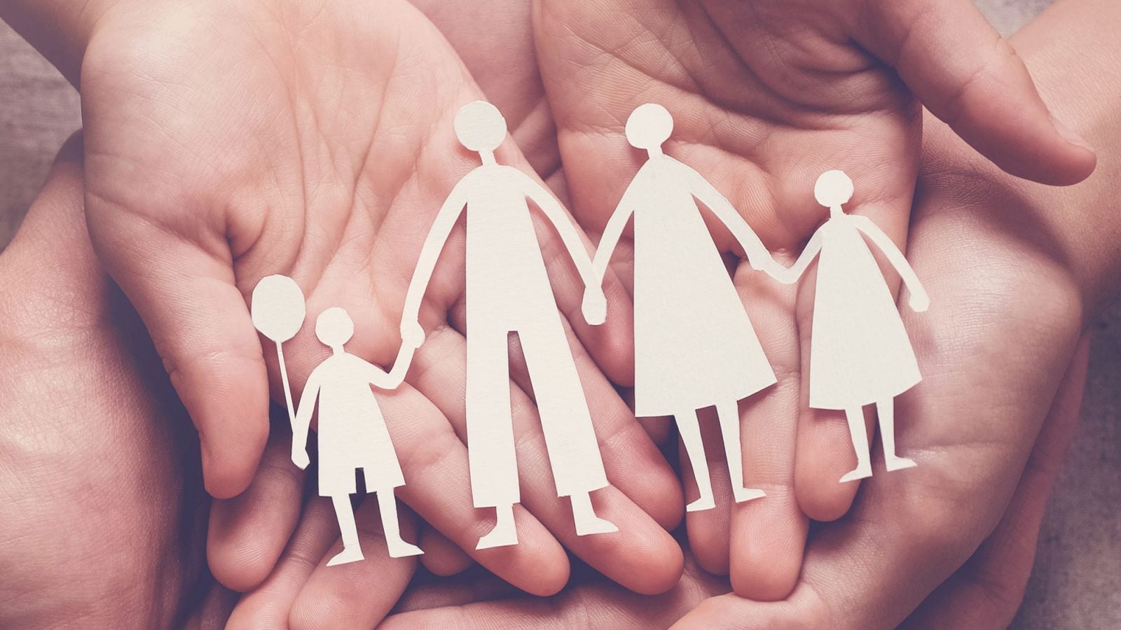 A pair of hands hold paper cutouts of a family of four.