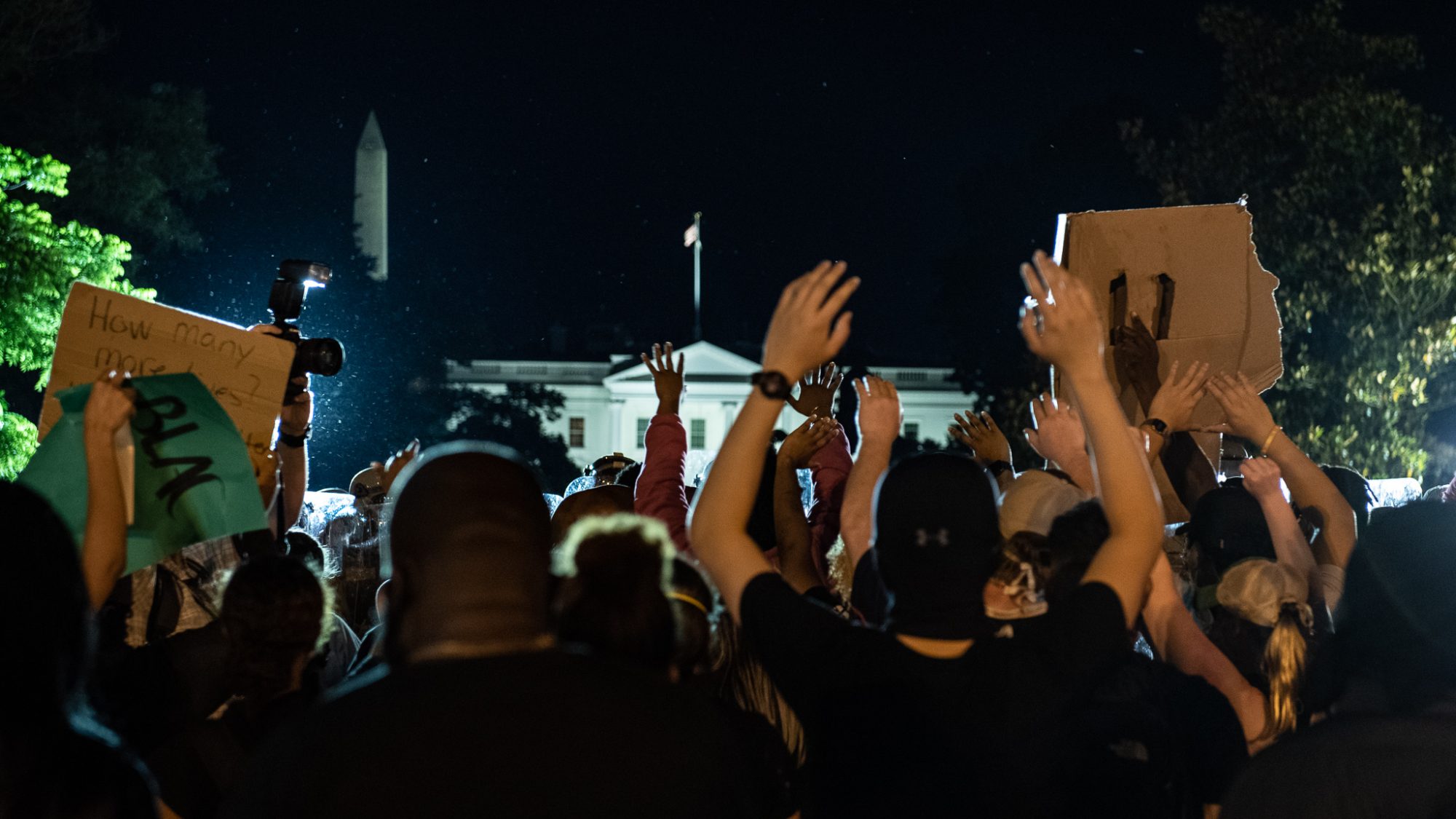 Racial justice protesters stand with their hands raised, with the White House in the background