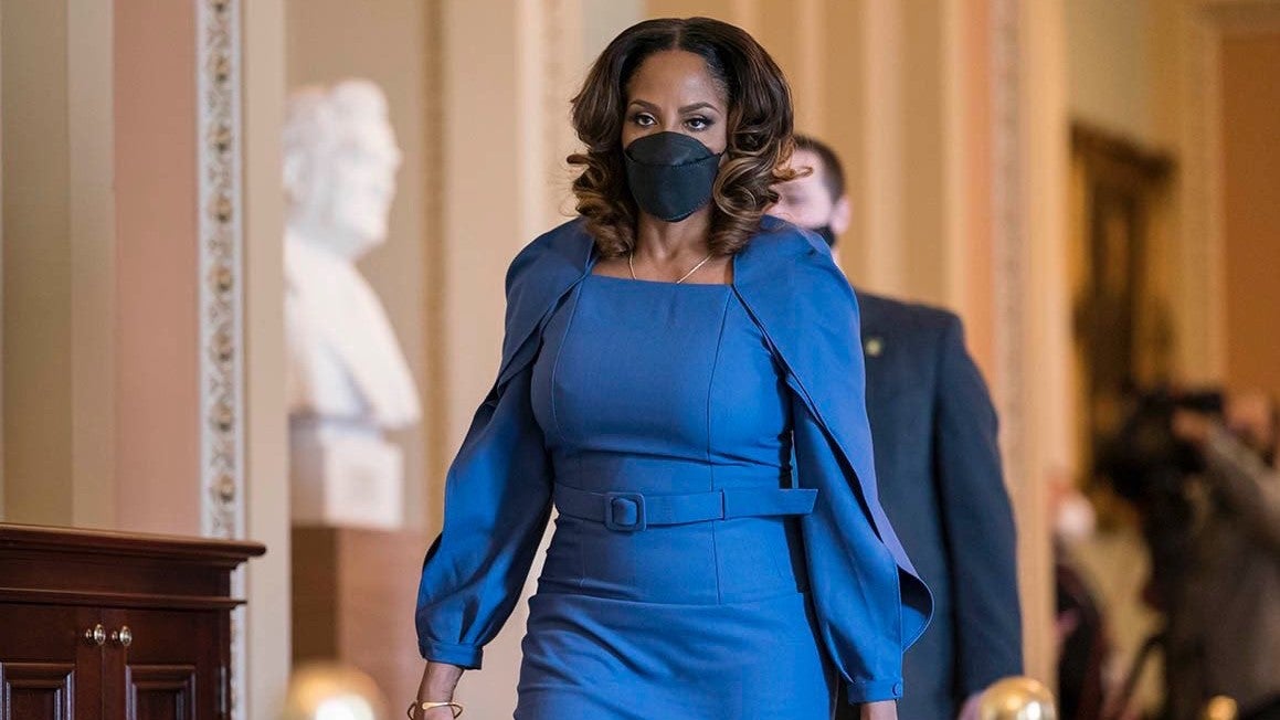 Stacey Plaskett, wearing a blue dress and black face mask, walks through the US Capitol