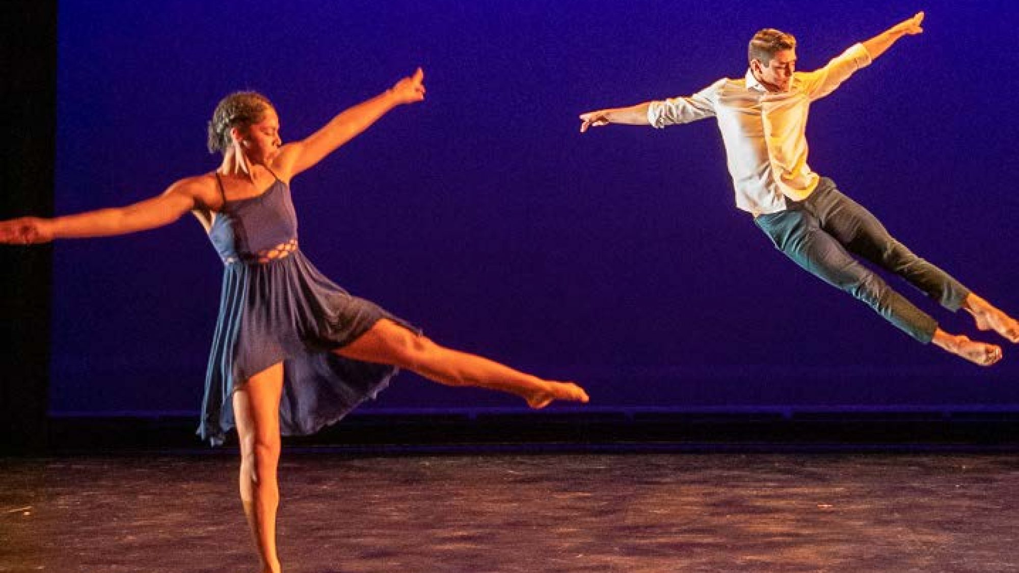 A duo of Black Movements Dance Theatre dancers leaps across the stage.