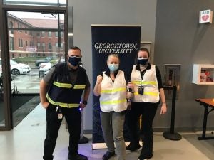 Marc Barbiere, Ranit Mishori, and Natalie Michalak wear vests in front of a Georgetown University sign