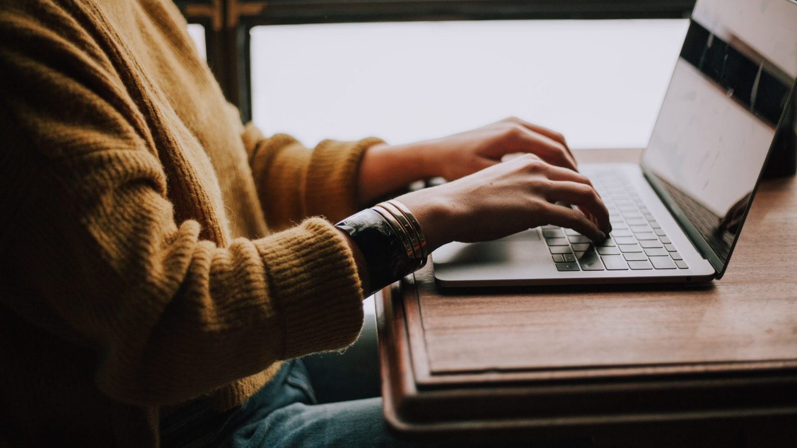 Woman wearing an orange sweater types on a laptop