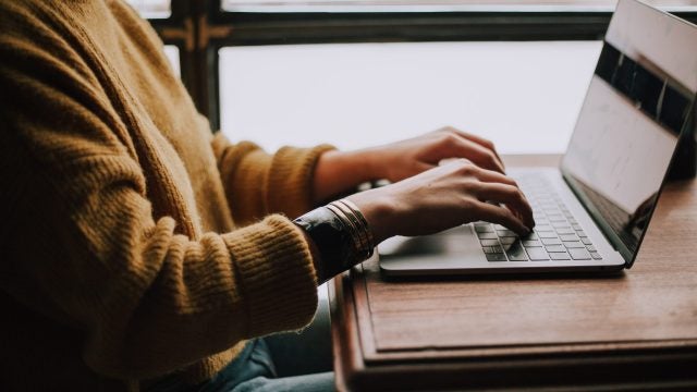 Woman wearing an orange sweater types on a laptop