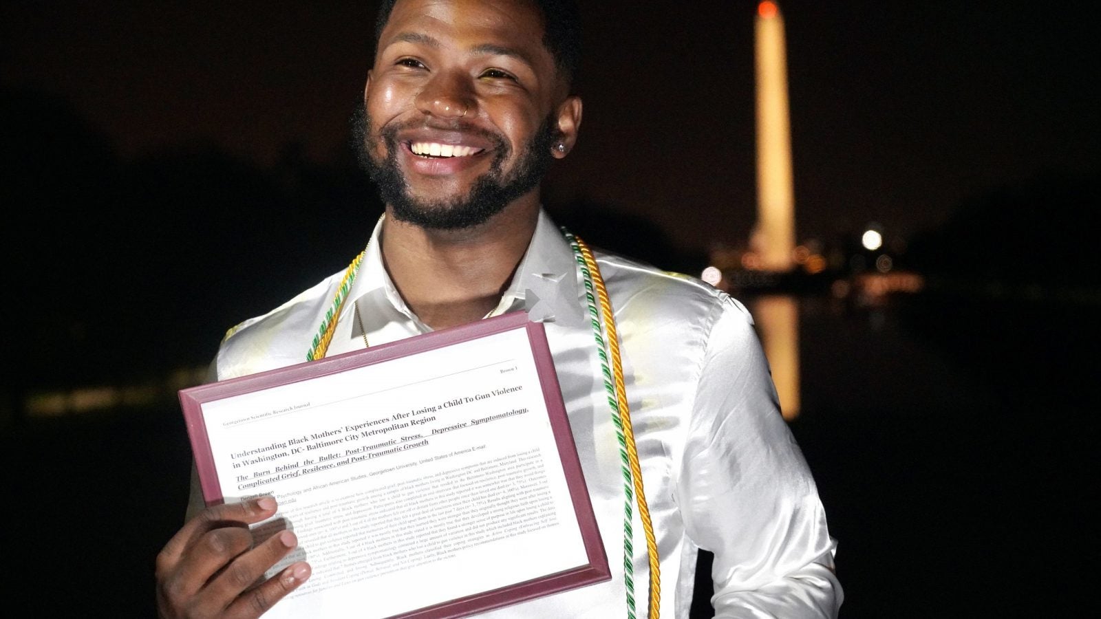 Denzell Brown holds his research in front of Washington Monument at night