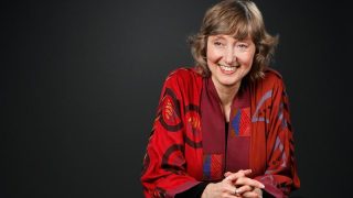 Deborah Tannen wears a red jacket in front of a black background