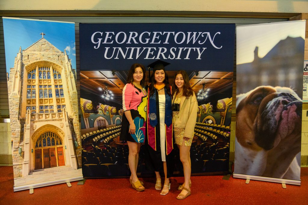 Graduate and two family members stand in front of a Georgetown University installation