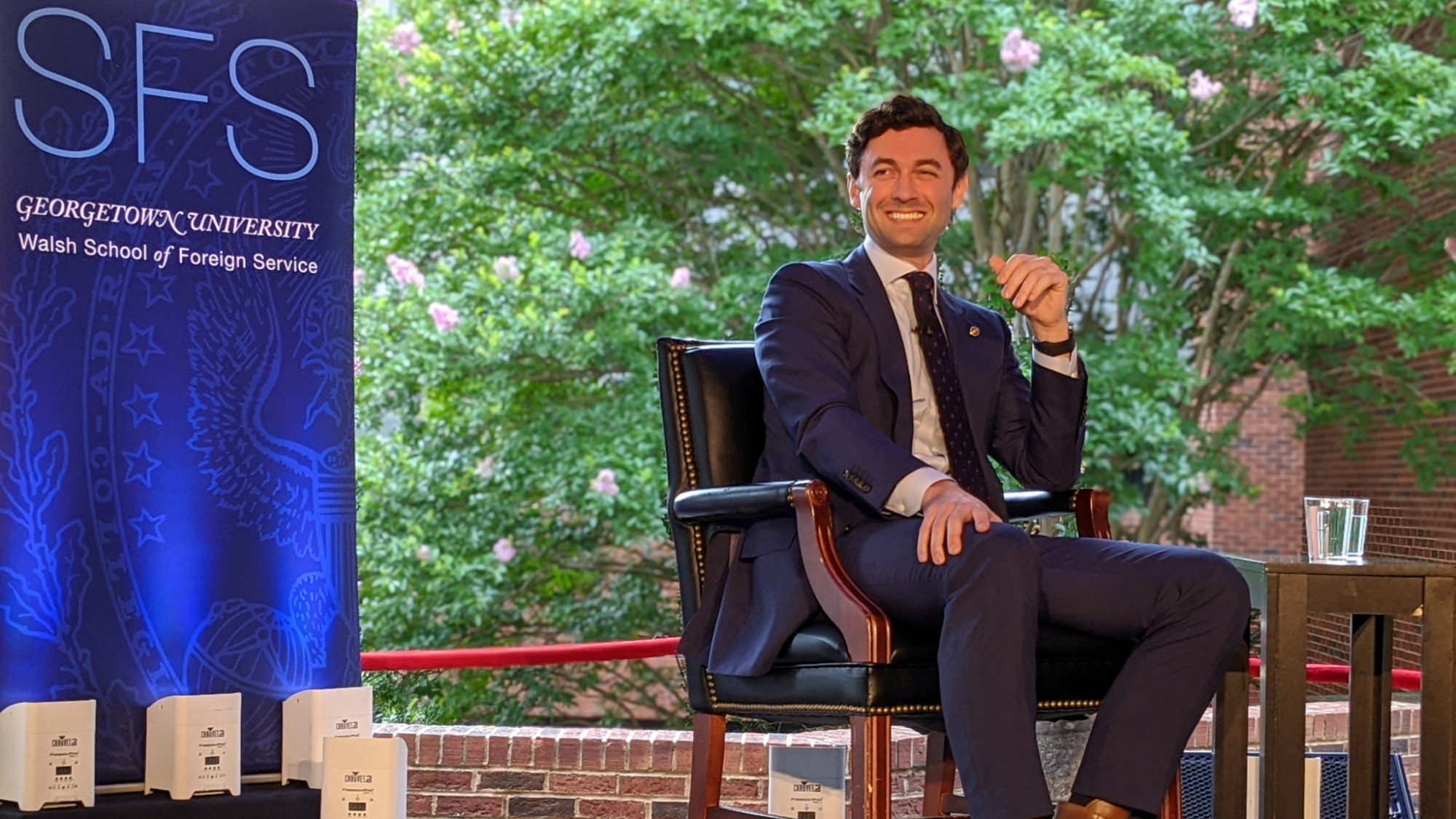 Sen. Jon Ossoff smiles while sitting outside near an SFS banner