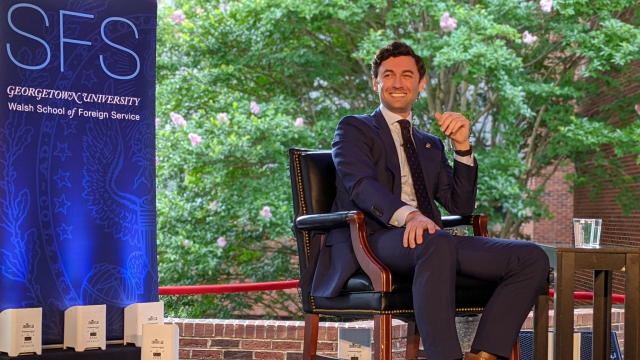 Sen. Jon Ossoff smiles while sitting outside near an SFS banner