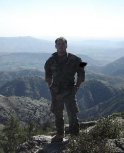 Timothy Torres wears camouflage and stands in front of mountains