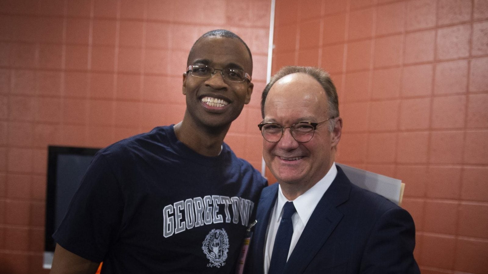 Joel Caston wears a Georgetown shirt and poses with Georgetown President John J. DeGioia