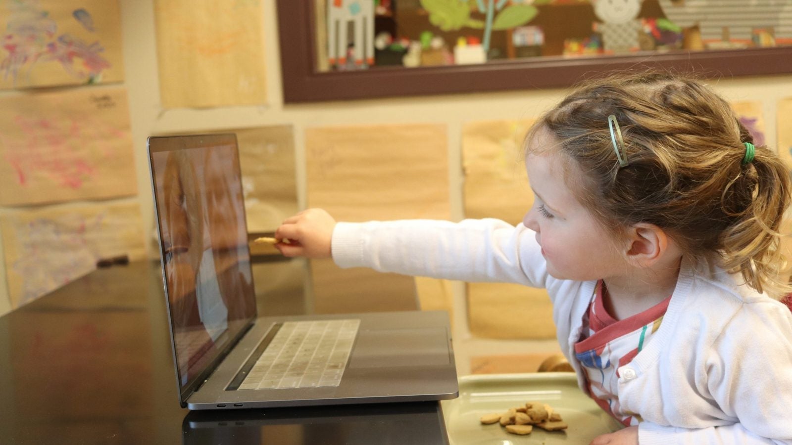 Blonde little girl reaches out to laptop screen