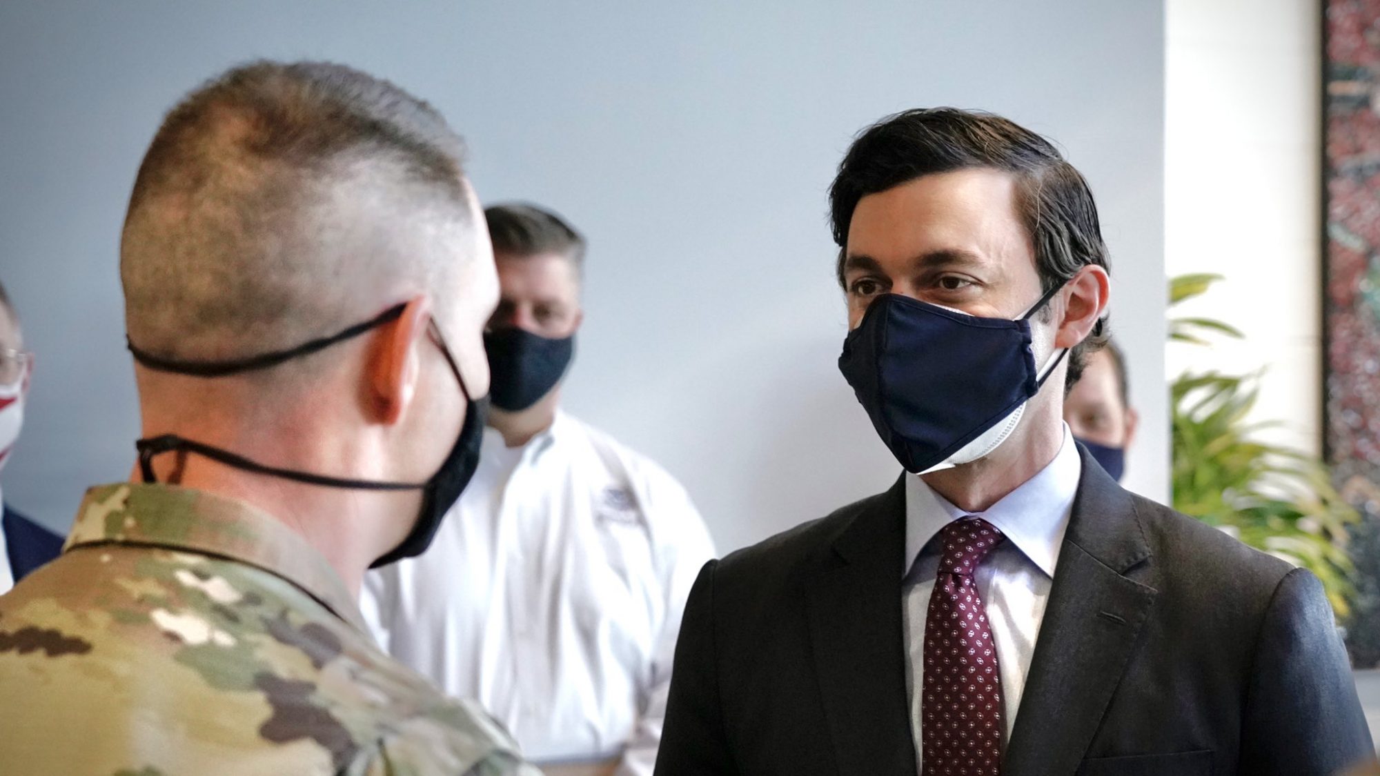 Sen. Jon Ossoff, wearing a black face mask, meets with a member of the military