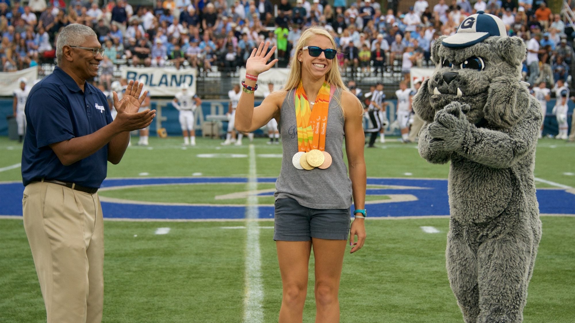 Lee Reed and the Bulldog mascot applaud a waving Michelle Konkoly wearing medals