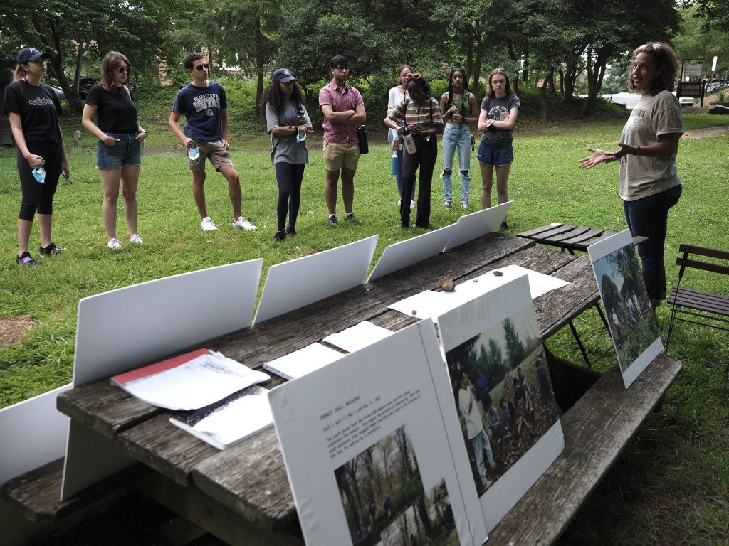 Students watch Lisa Fager present using multiple posters leaning against a table