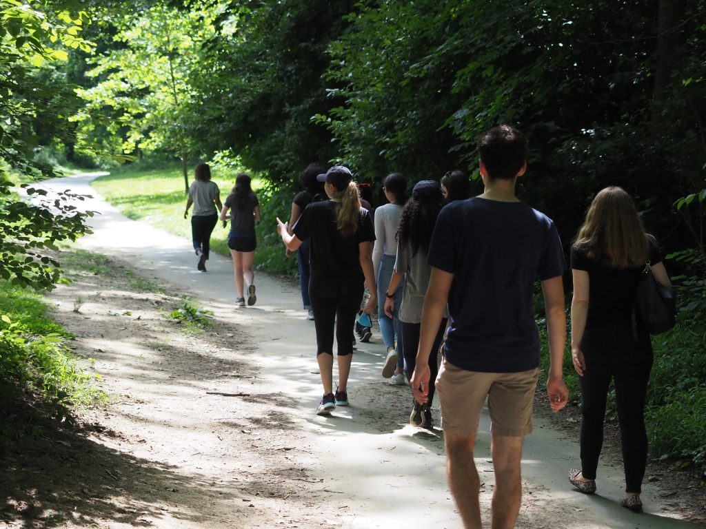 Students following a tour guide walking along a wooded path