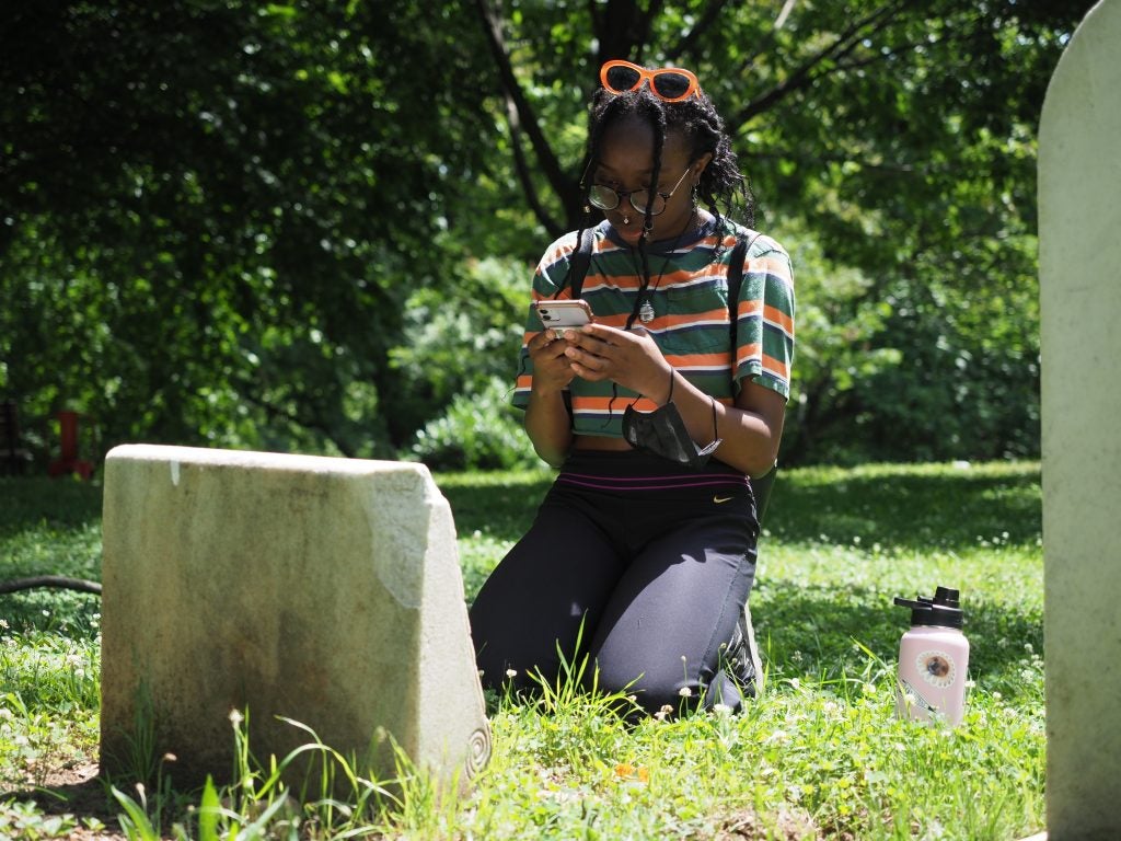 Student works on her phone kneeling in front of a headstone