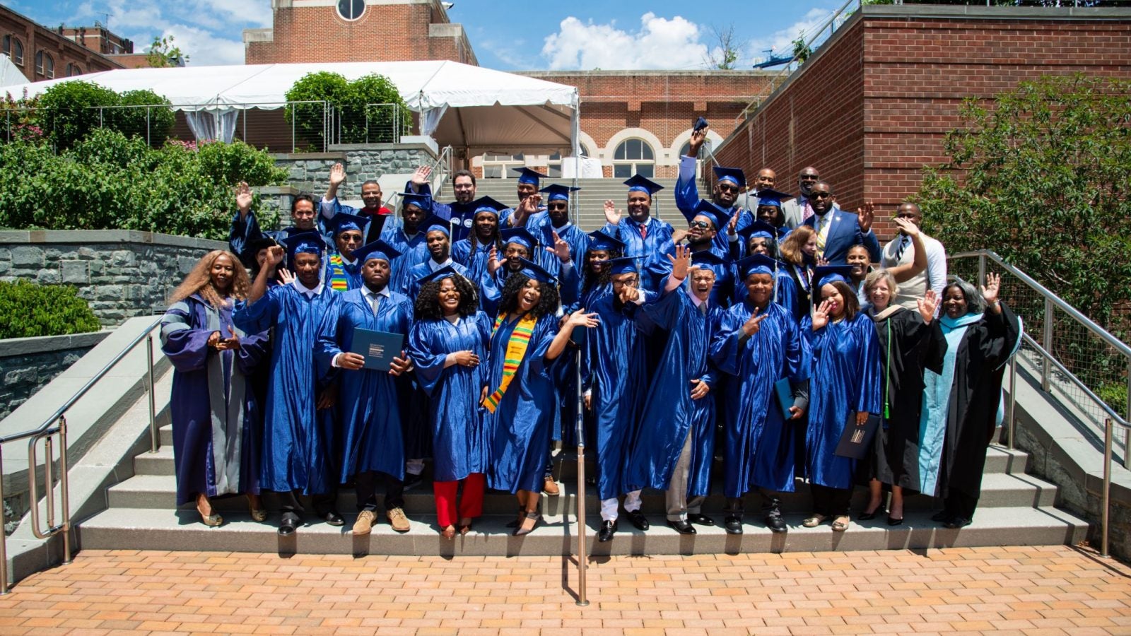 Students in blue graduation robes stand on steps next to Regents Hall