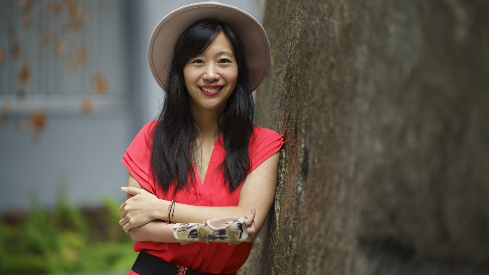 Tiffany Yu wears a hat and pink dress while leaning against a tree