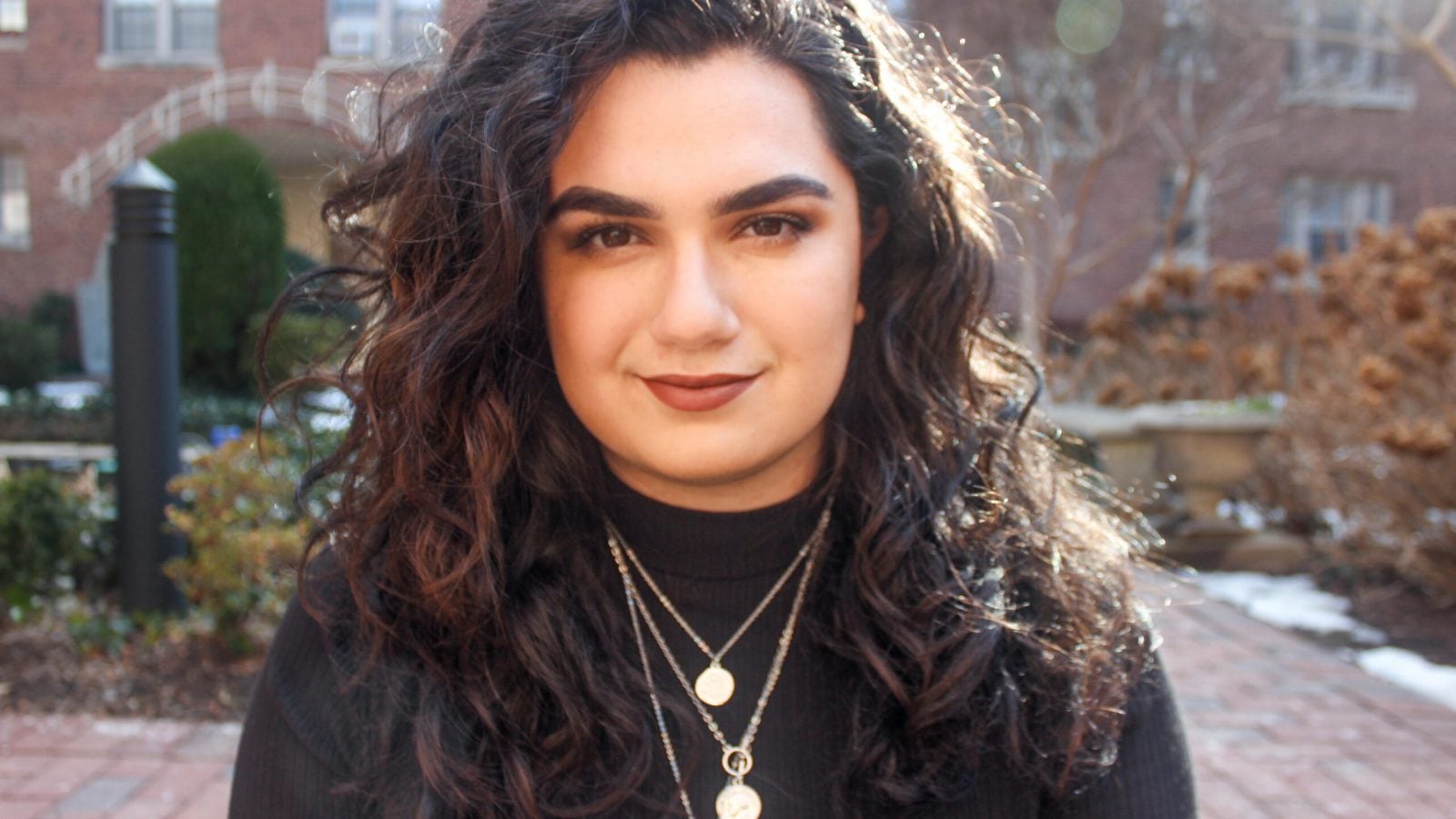 Headshot of Alanna Kronk with brick patio and buildings in the background