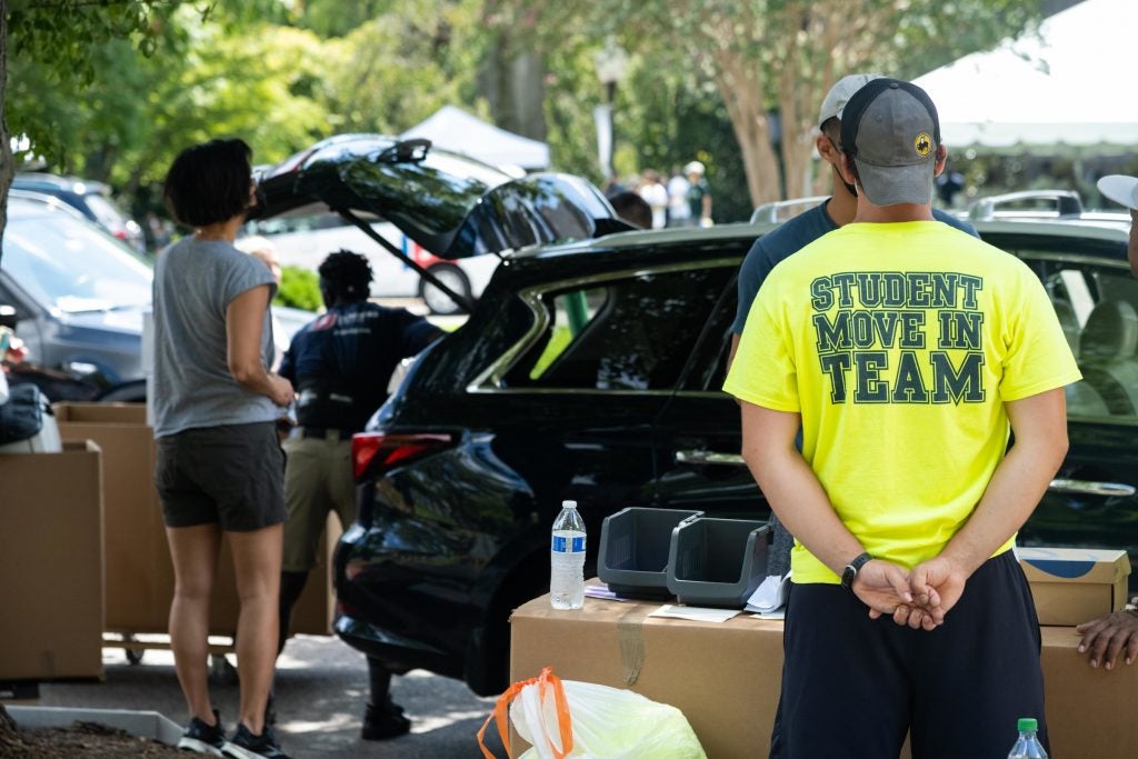 Student wearing a neon "Student Move In Team" t-shirt helps new students unload their car