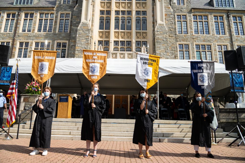 Students wearing robes hold flags on a pole outside