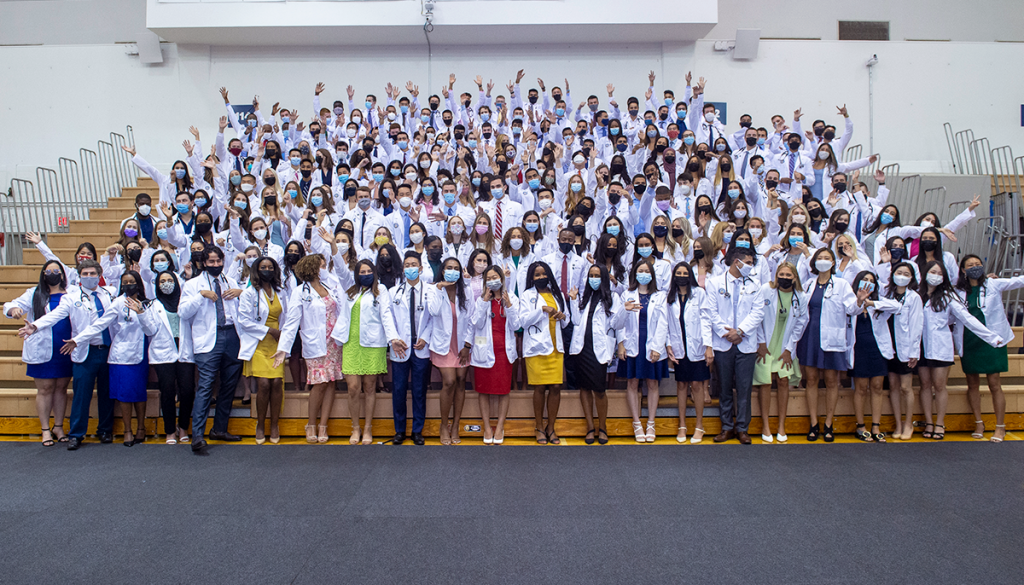 Medical students wear white coats pose for a photo on bleachers