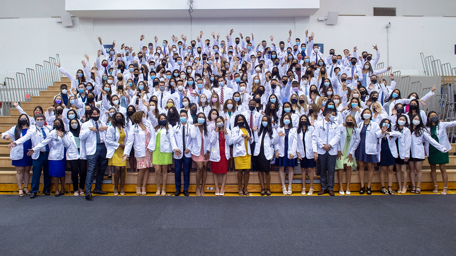 Medical students wear white coats pose for a photo on bleachers