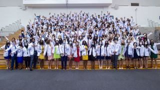 Medical students wear white coats pose for a photo on bleachers