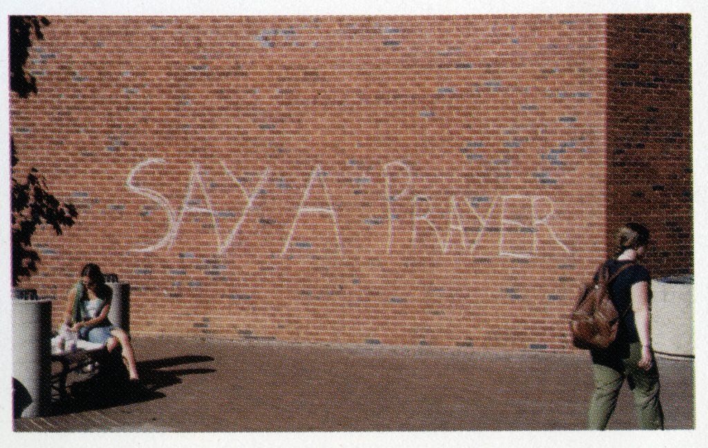 "Say a Prayer" written in chalk on a brick building