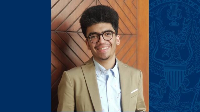 Antony Costantin wears a tan blazer and glasses in his headshot