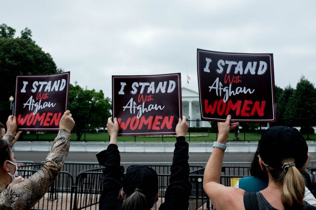 Women holding signs that say "I stand with Afghan Women" in front of the White House