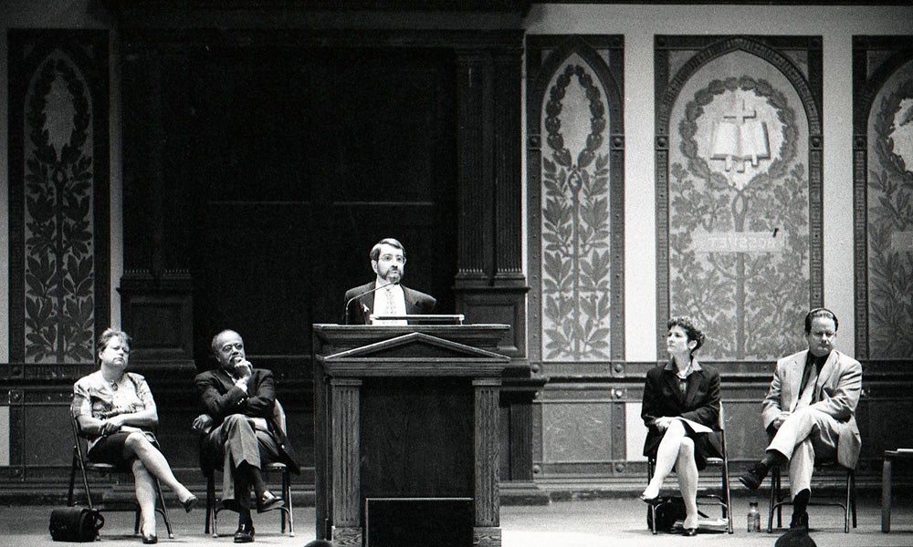 Black and white image of five administrators speaking from a stage