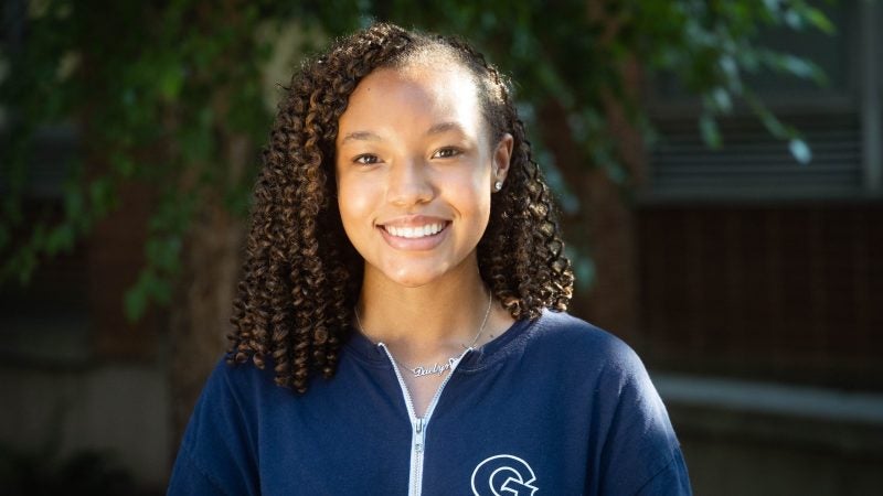 Daelyn Waters wearing a dark blue Georgetown zip up outside in front of a tree