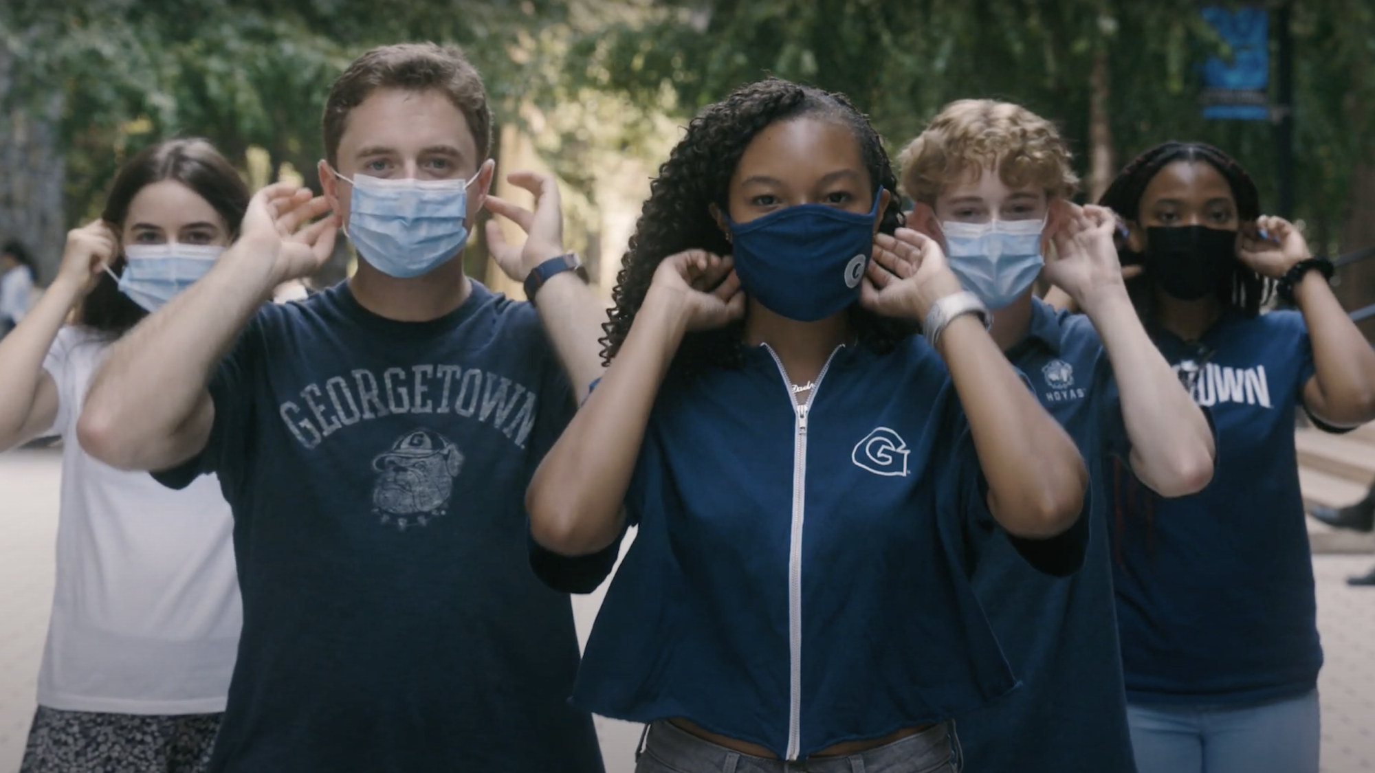 Five students wearing Georgetown apparel put on their masks