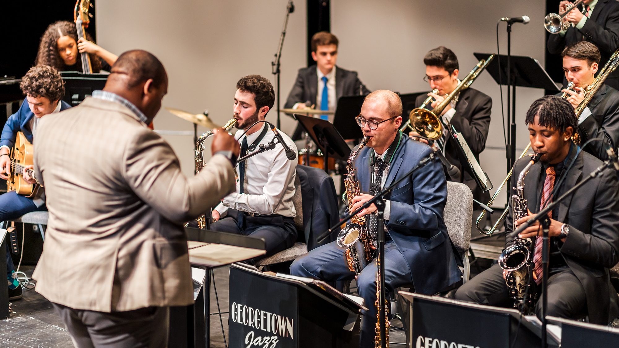Prof. Paul Bratcher conducts the GU Jazz Ensemble students, including bass player at left, saxophones to right.