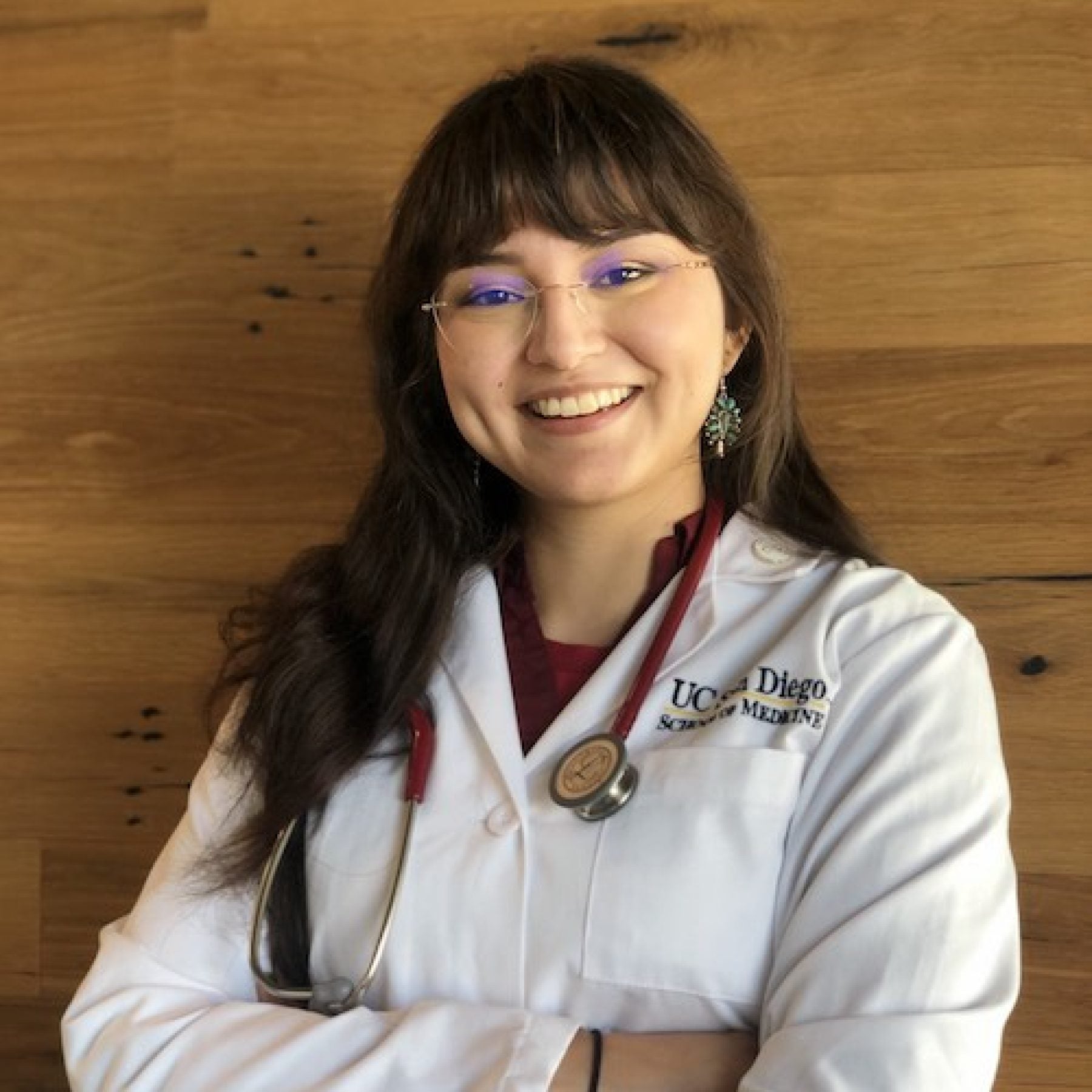 Yasmin Zuch smiles while folding her arms wearing a doctor&#039;s white coat and glasses