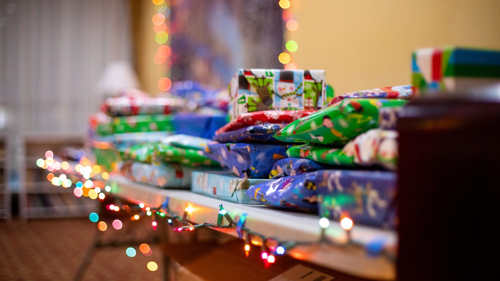 Wrapped gifts on a table with a string of multi-color lights