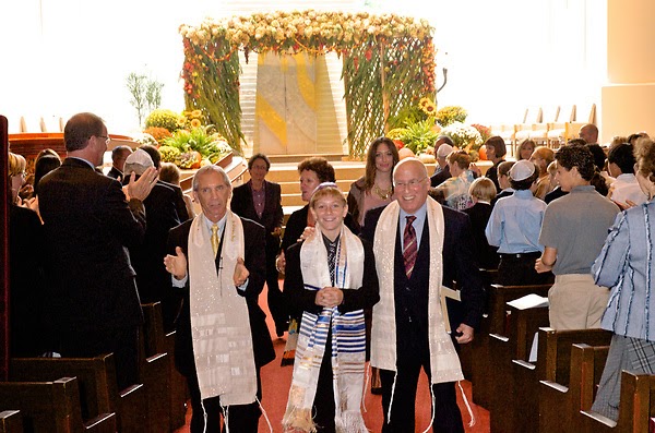 Young Ari Filler walking with his rabbi, cantor and family down an aisle