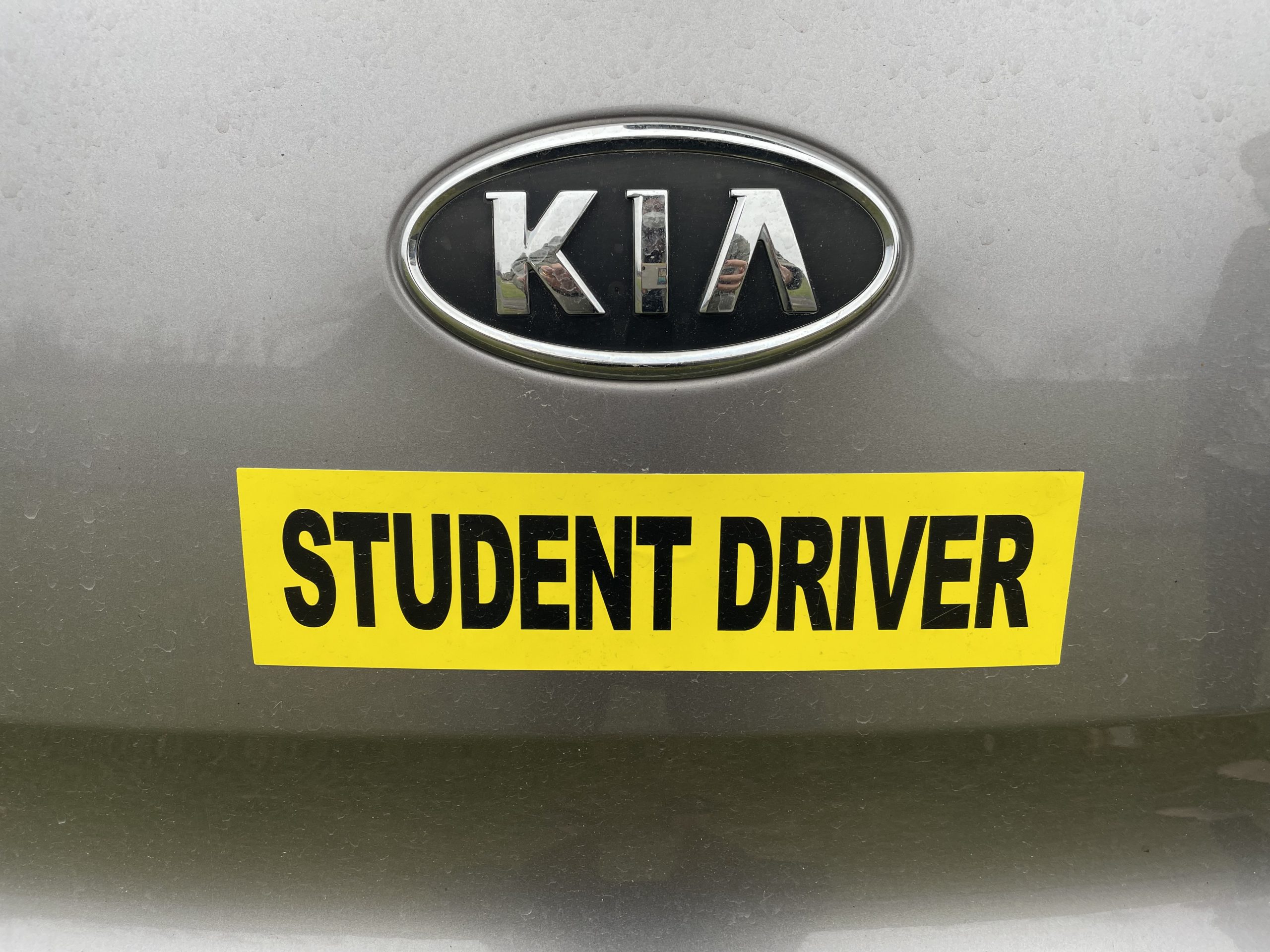 Bumper sticker that says "Student Driver" under a Kia car logo