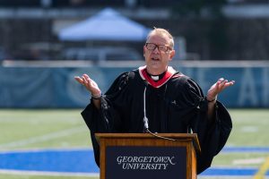 Fr. Greg delivers a speech from behind a podium on Cooper field