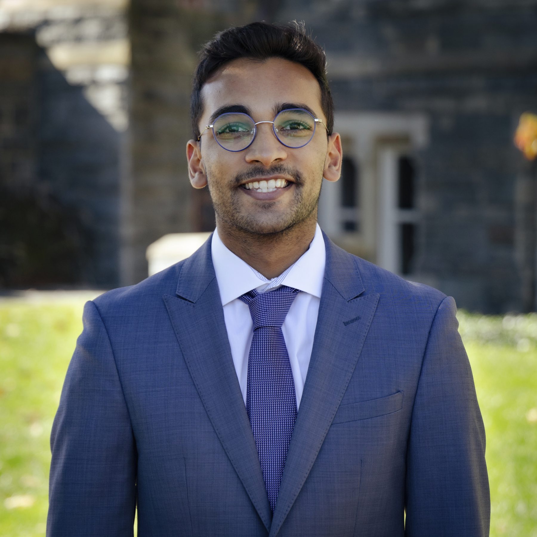 Arjun Ravi wears glasses and a light blue suit for a headshot outside