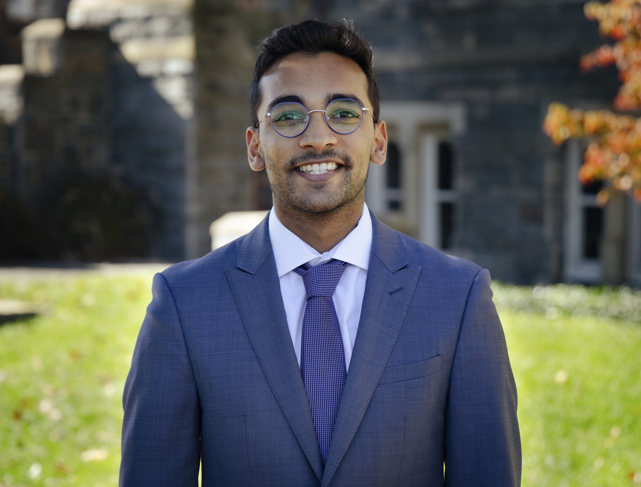 Arjun Ravi wears glasses and a light blue suit for a headshot outside