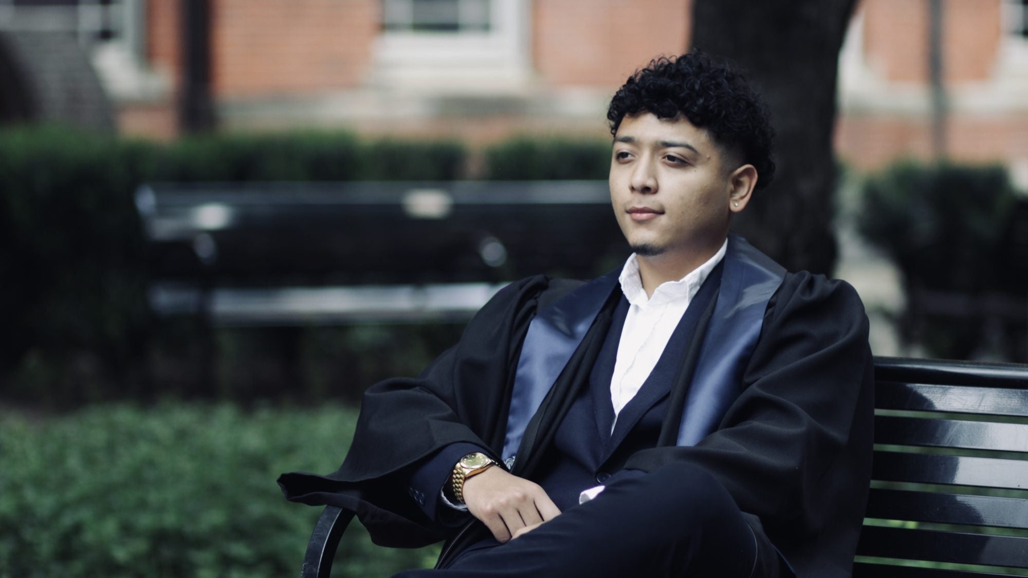 Andy sits on a bench in Dahlgren Quad in his graduation robes