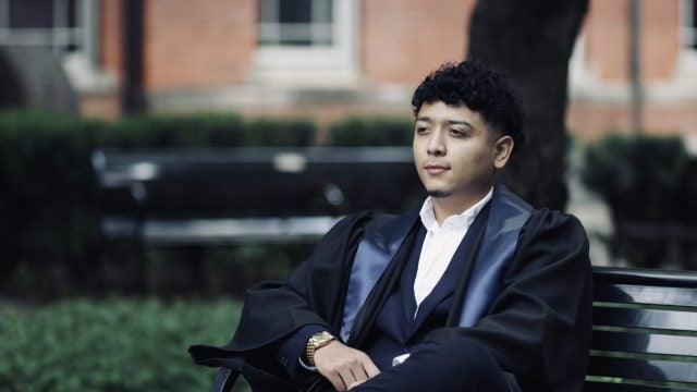 Andy sits on a bench in Dahlgren Quad in his graduation robes