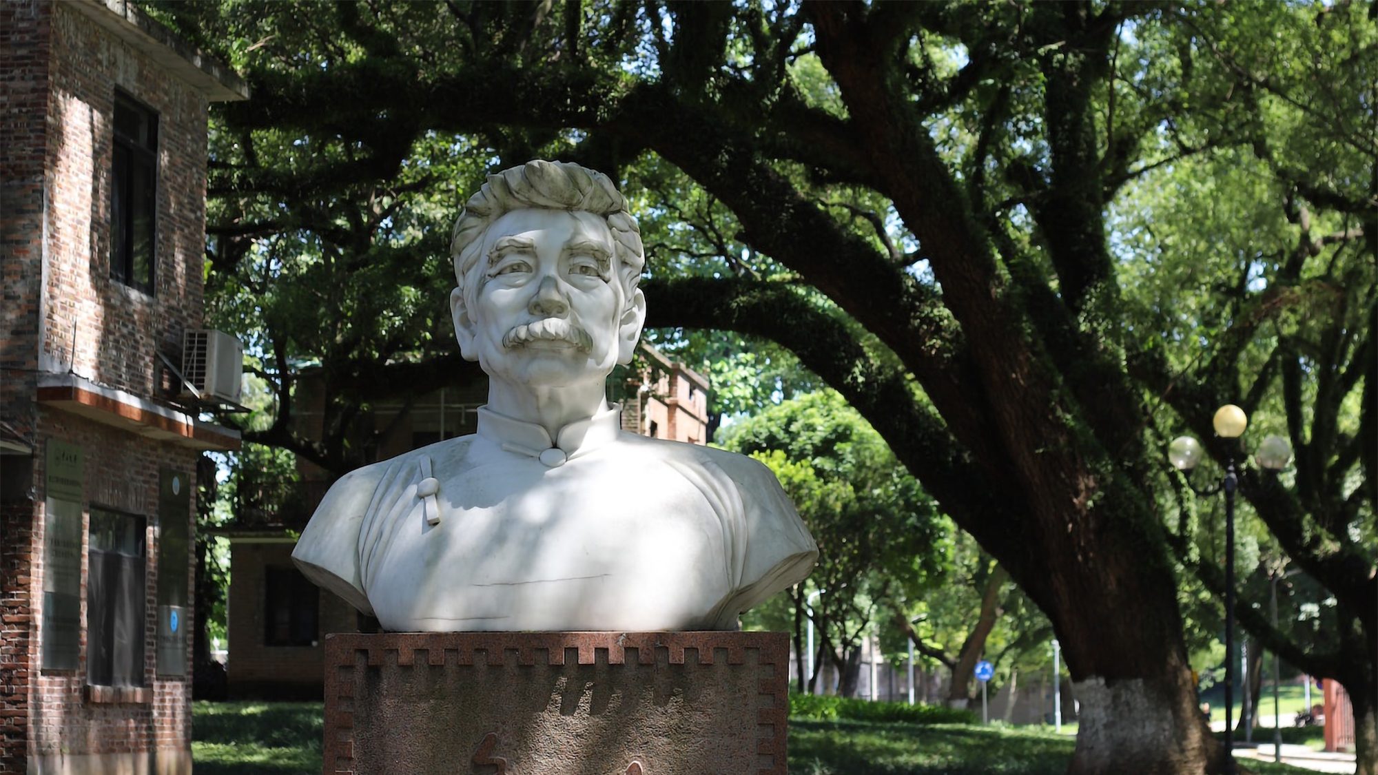 Statue bust of Lu Xun with leafy trees in background