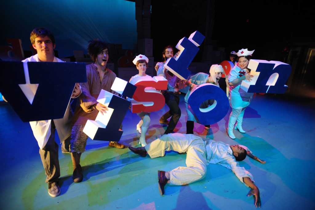 Actors dressed as medical professionals and patients hold large letters spelling out "vision"