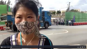 Natsu Onoda Power wears a mask and headphones in front a truck and protesters