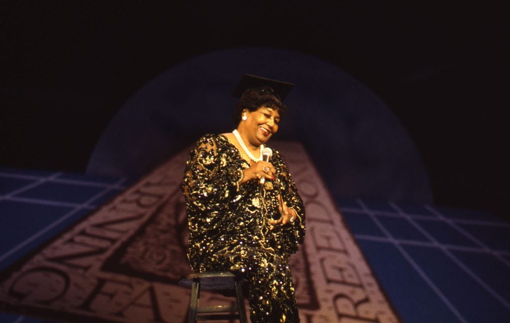 Pearl Bailey wears a graduation cap and sings into a microphone