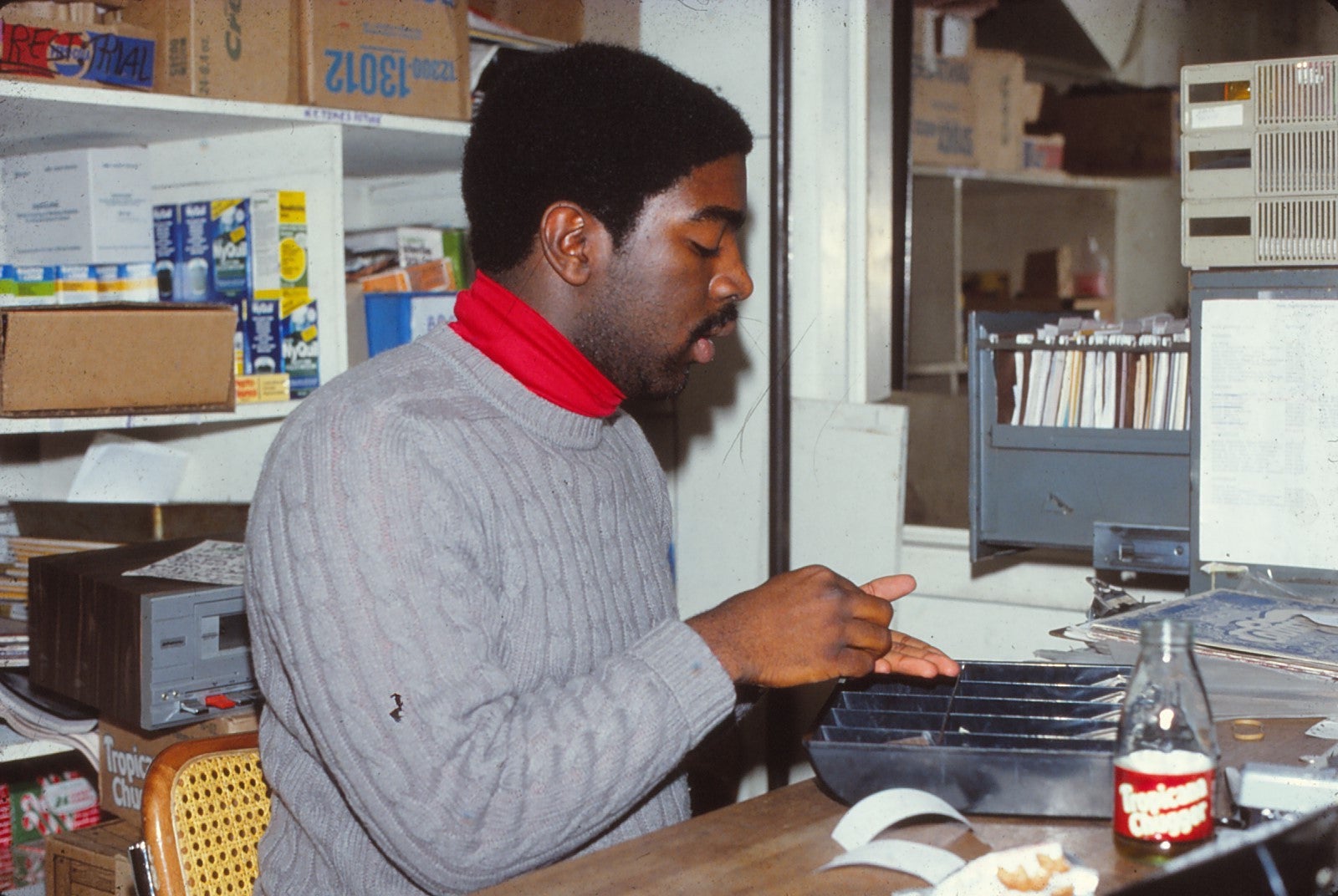 Young man in a gray sweater with red shirt underneath at a desk